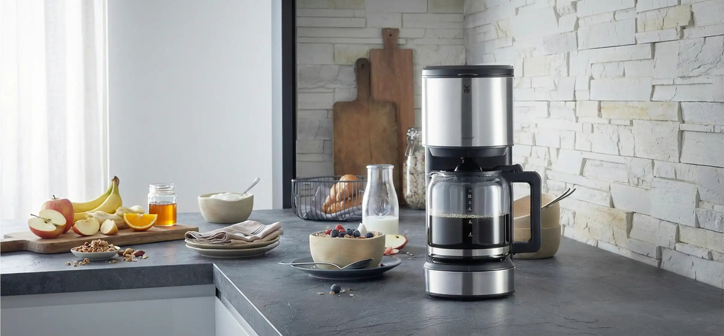 Kaffeemaschine auf Küchentresen mit Müslischale und Obst im Hintergrund