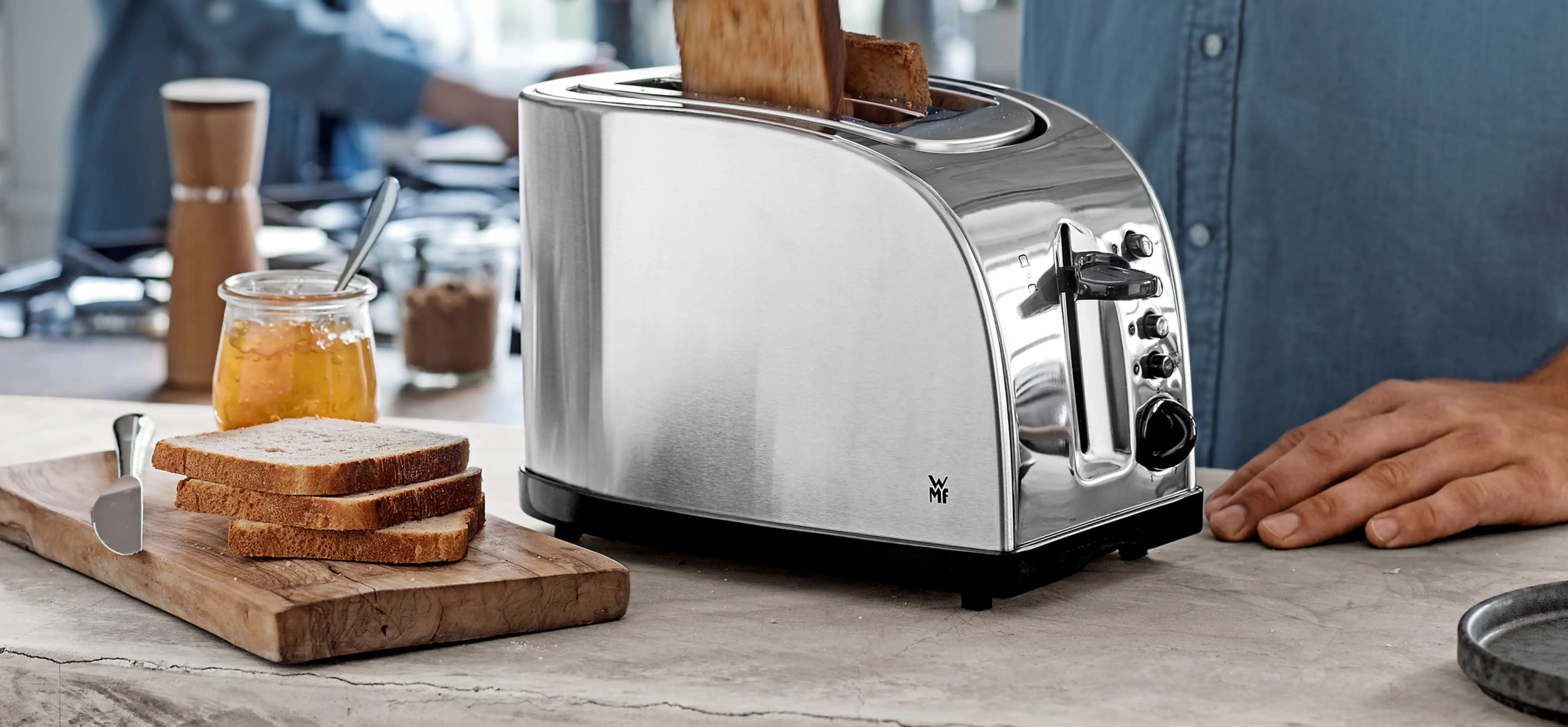 Toaster in silber mit heraustragendem Toast. Daneben Holzbrett mit Toast und Honig