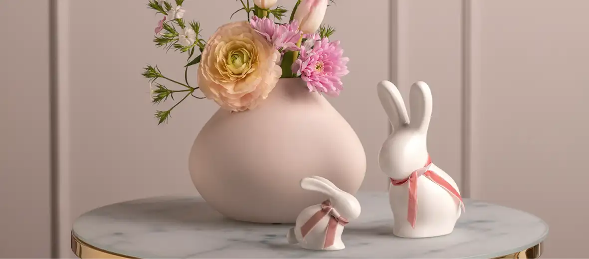 Osterhasen aus Keramik aus Beistelltisch, dahinter Vase in rosa mit bunten Blumen