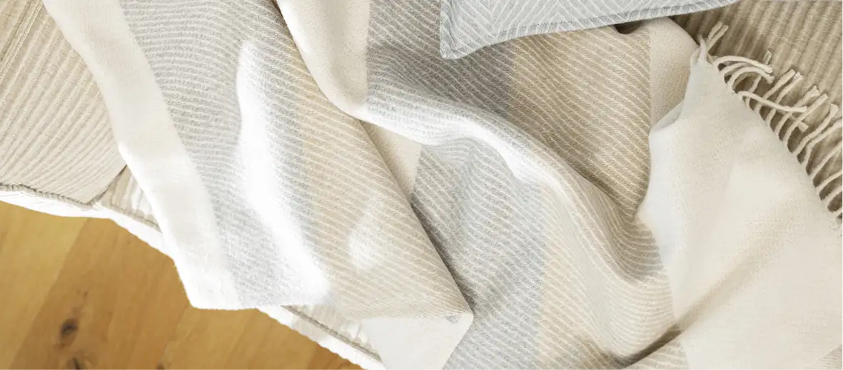 Dünne Decke in beige, grau und weiß auf dem Boden liegend