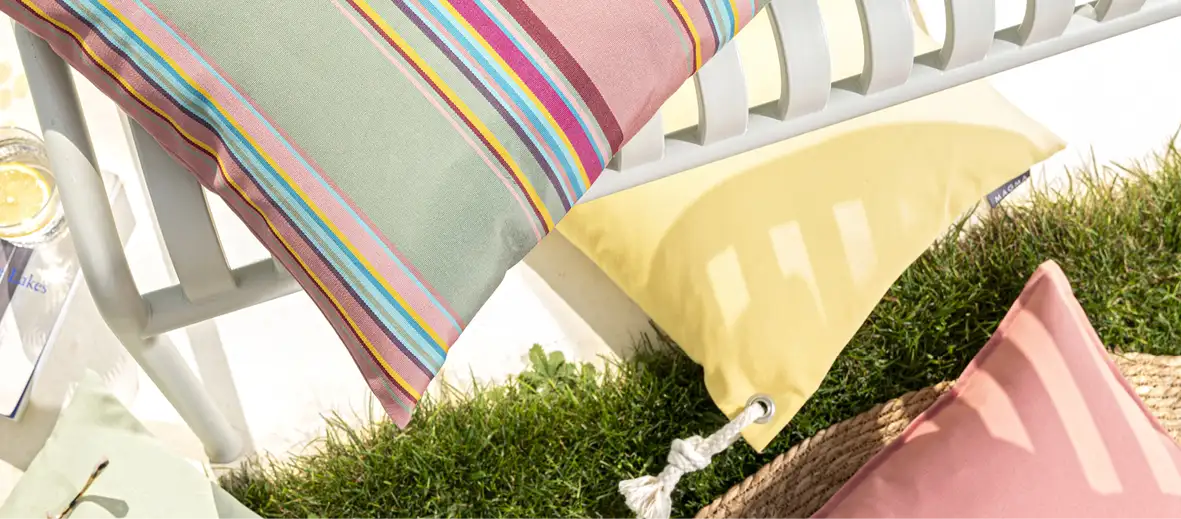 Kissen in rosa, blau und gelb auf weißer Bank im Gras