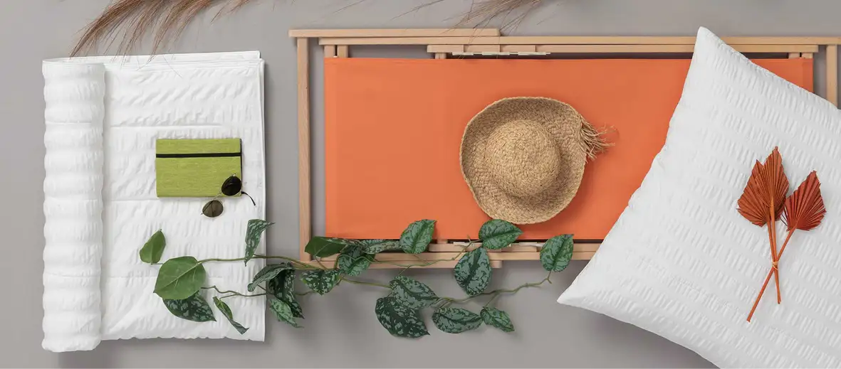 Sommerdecke gerollt daneben Liege in orange und Kissen. Sonnenhut und Pflanzen