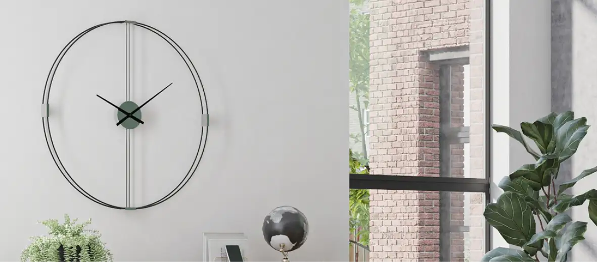 Wanduhr aus schwarzem Rahmen an der Wand, daneben Fenster und Pflanzen