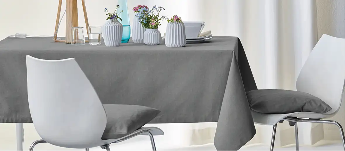 Tischdecke in grau auf Tisch mit Stühlen. Auf dem Tisch stehen kleine Vasen